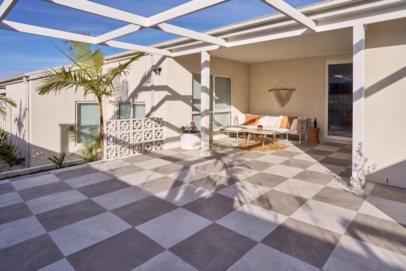 Checkerboard paving under a white pergola with a lounge setting